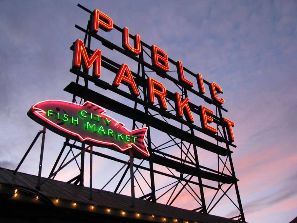 Neon signs for "Public Market" and "City Fish Market" with an outline of a fish, set against a twilight sky.