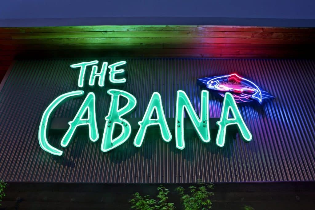 Neon sign reading "The Cabana" with a glowing fish outline on a textured wall.