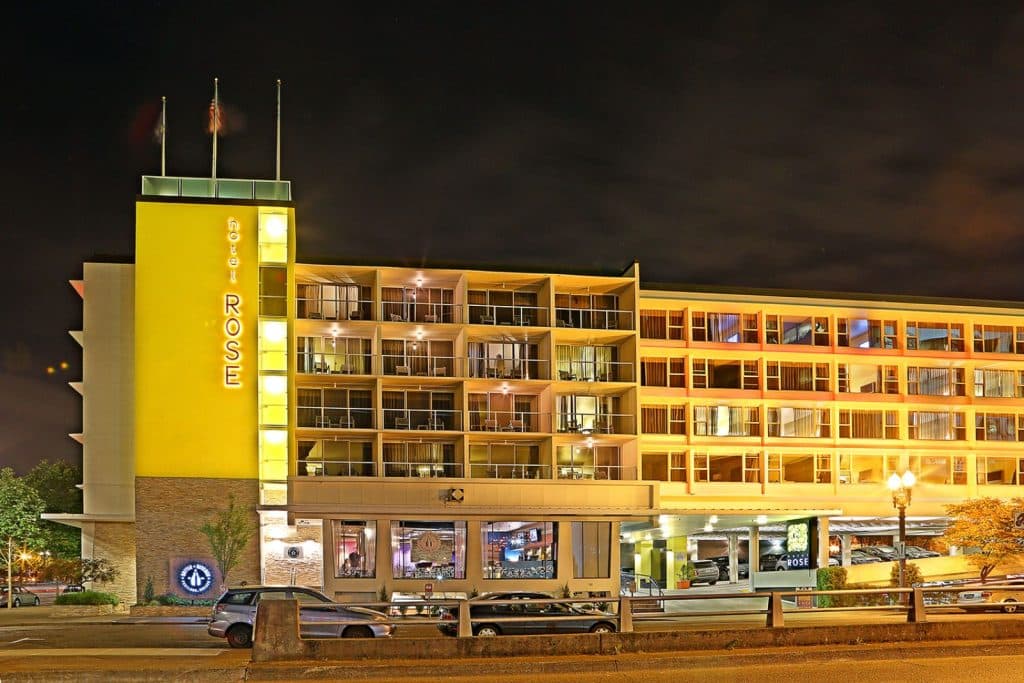 Night view of Hotel Rose, a multi-story building with illuminated signage and balconies, surrounded by city lights.