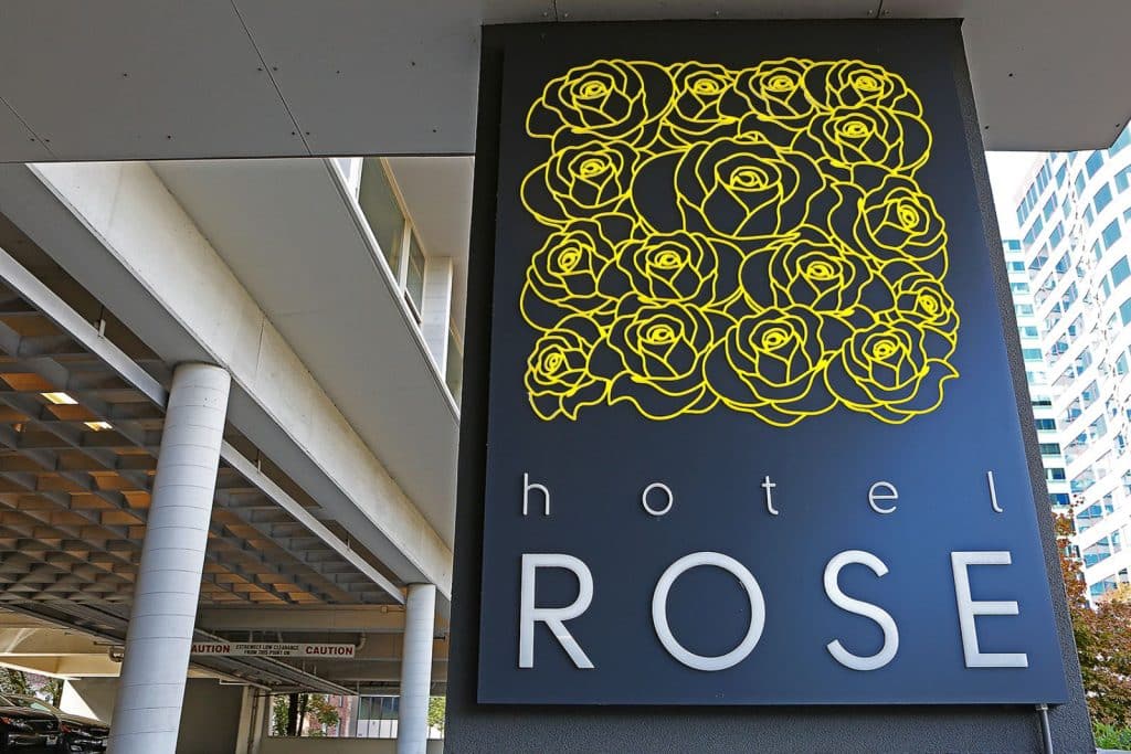 Sign for Hotel Rose featuring a black background with a pattern of yellow roses and the words "hotel ROSE" beneath. The building is visible in the background.