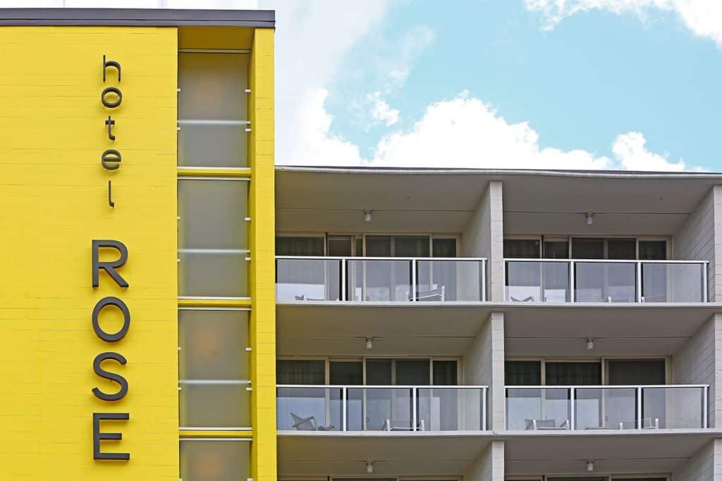 Yellow exterior of Hotel Rose with vertical sign and balconies, set against a partly cloudy sky.