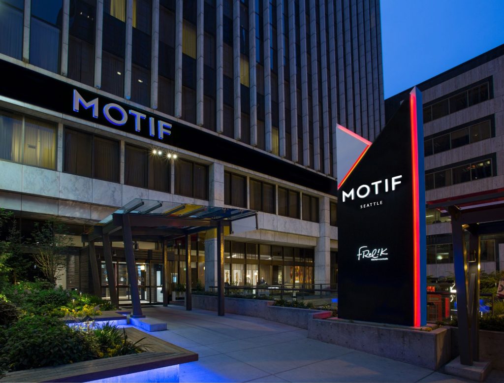 Exterior view of the Motif Seattle hotel entrance, featuring modern architecture and illuminated signage during evening.