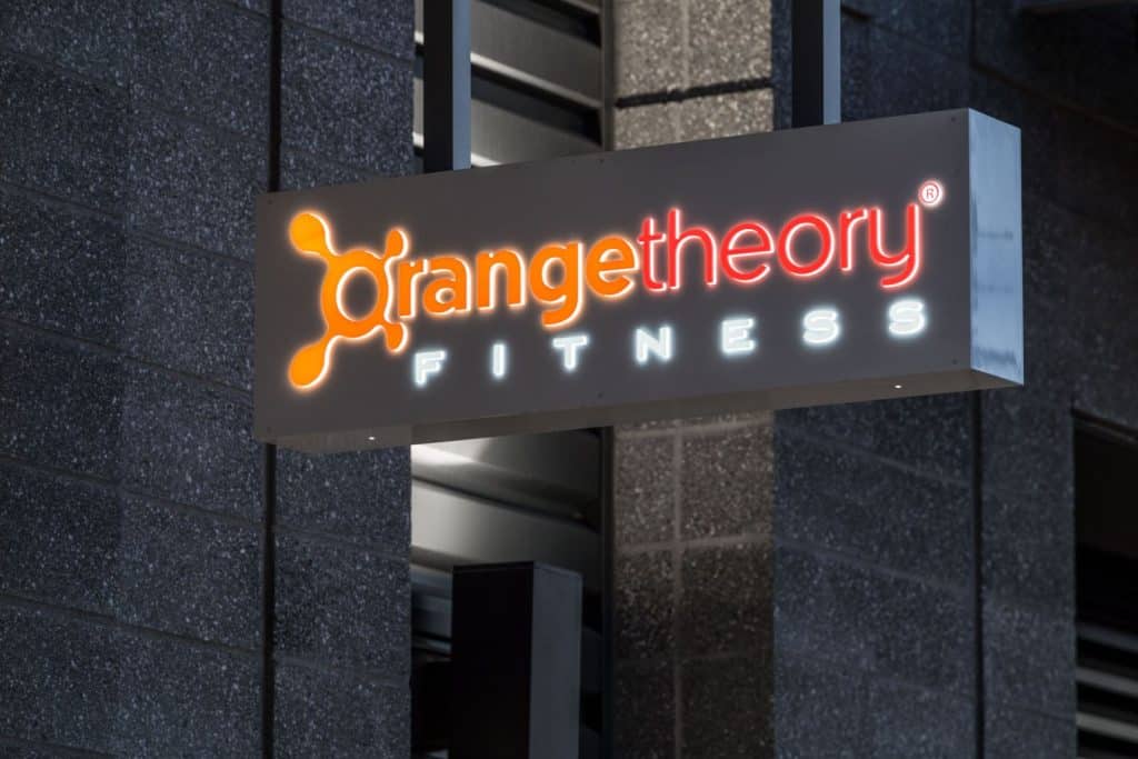 A lit sign reading "Orangetheory Fitness" is mounted on a building wall.