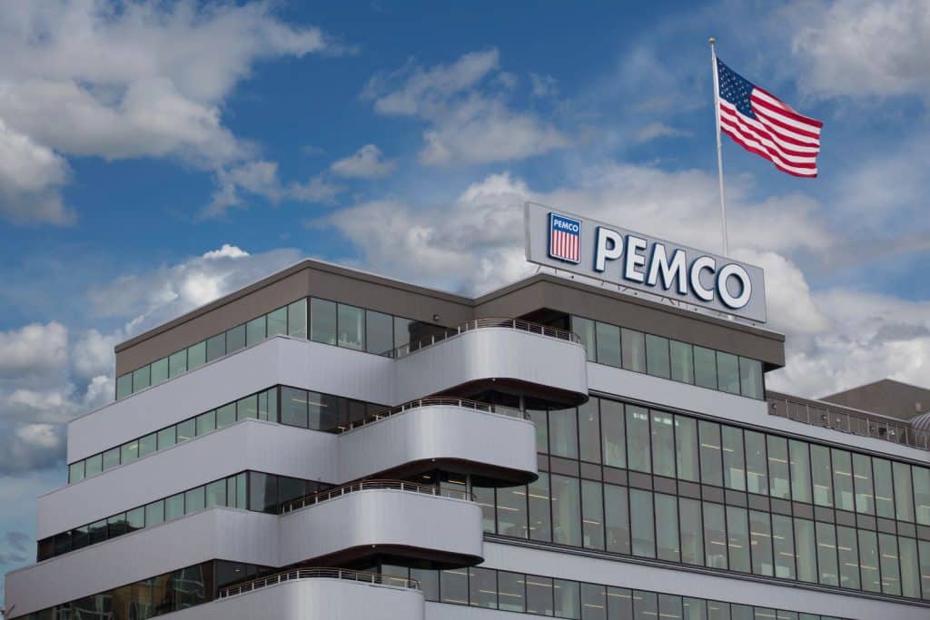 A modern office building with a PEMCO sign on the roof and an American flag, set against a cloudy blue sky.