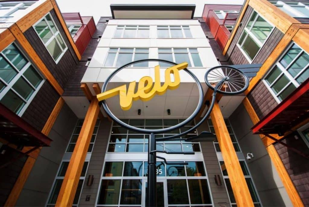 Entrance of a modern building with a sign reading "velo" shaped like a bicycle wheel.