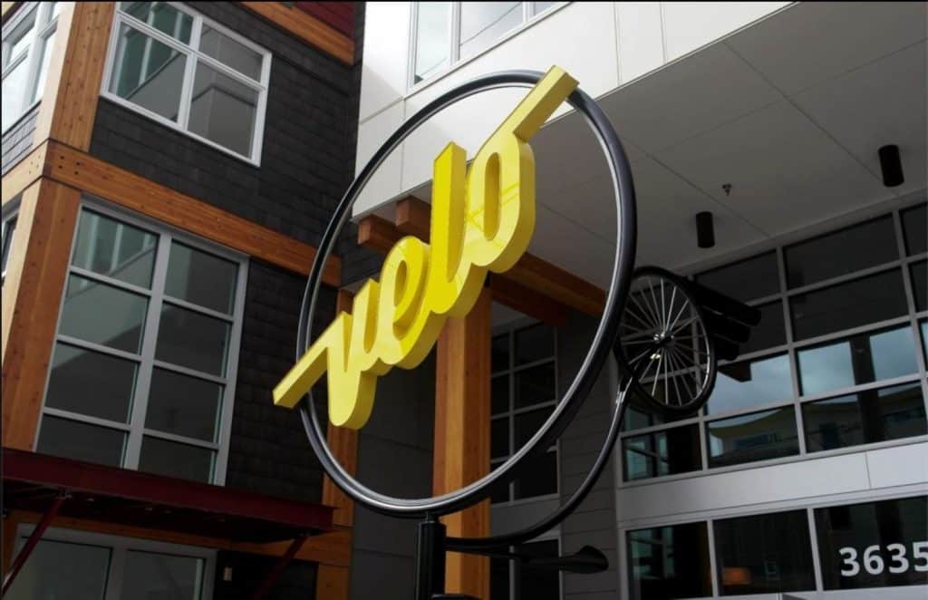 Yellow "Velo" sign with a bike wheel decor against a modern building facade.