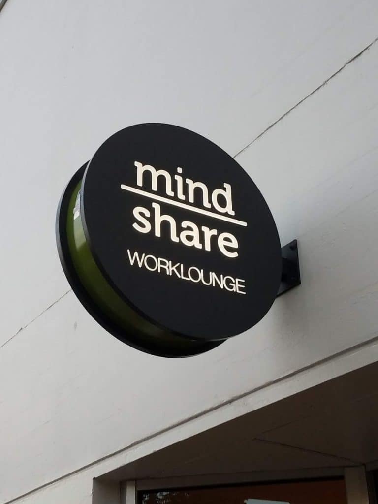 A round black sign on a building reads "mind share WORKLOUNGE" in white text.