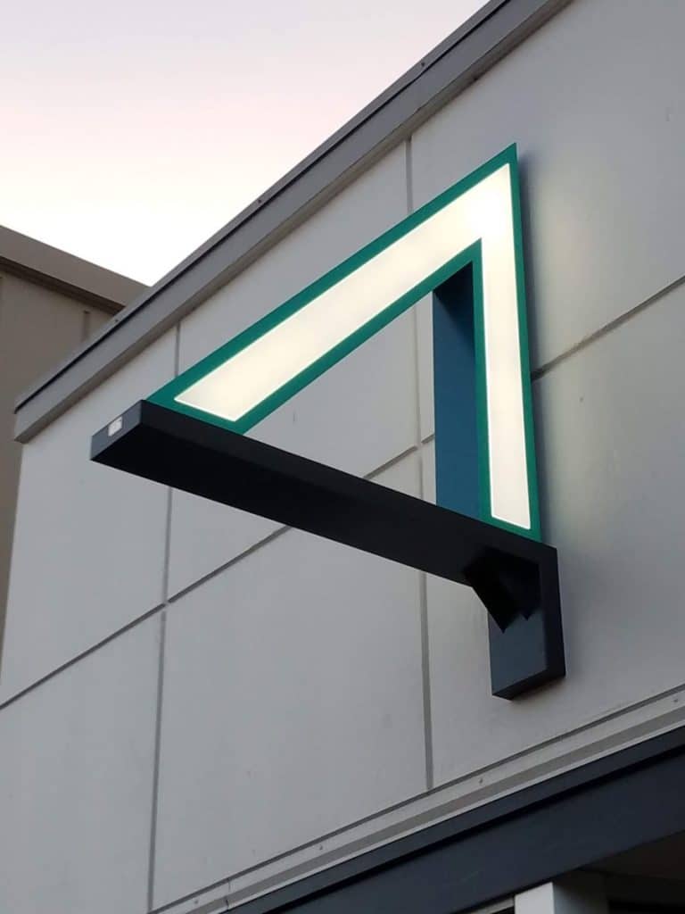 A triangular, illuminated sign with a modern design is mounted on the exterior of a building.