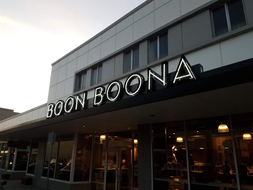 Exterior view of Boon Boona coffee shop with illuminated sign and large windows.