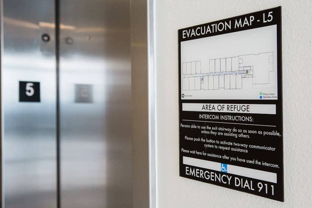 Evacuation map and instructions on wall next to elevators. Sign provides emergency information and intercom instructions for floor L5.