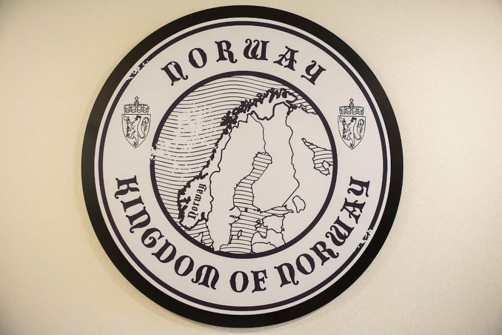 Round emblem with a map of Norway in the center, surrounded by the text "Kingdom of Norway" and illustrations of crowns.