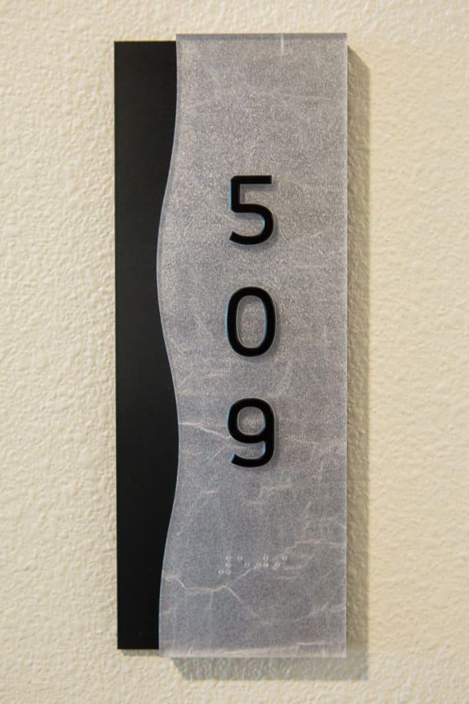 A room number sign displaying "509" in large black numbers on a textured gray background with a black vertical stripe on the left. Braille is included beneath the numbers.