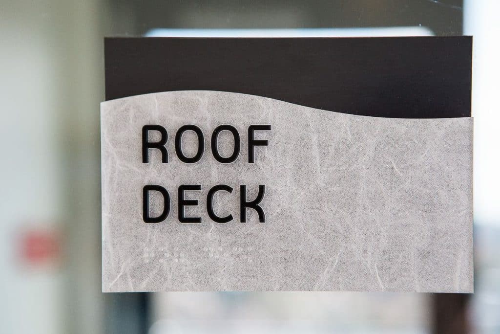 Sign reading "Roof Deck" with a textured gray background and a black stripe at the top.