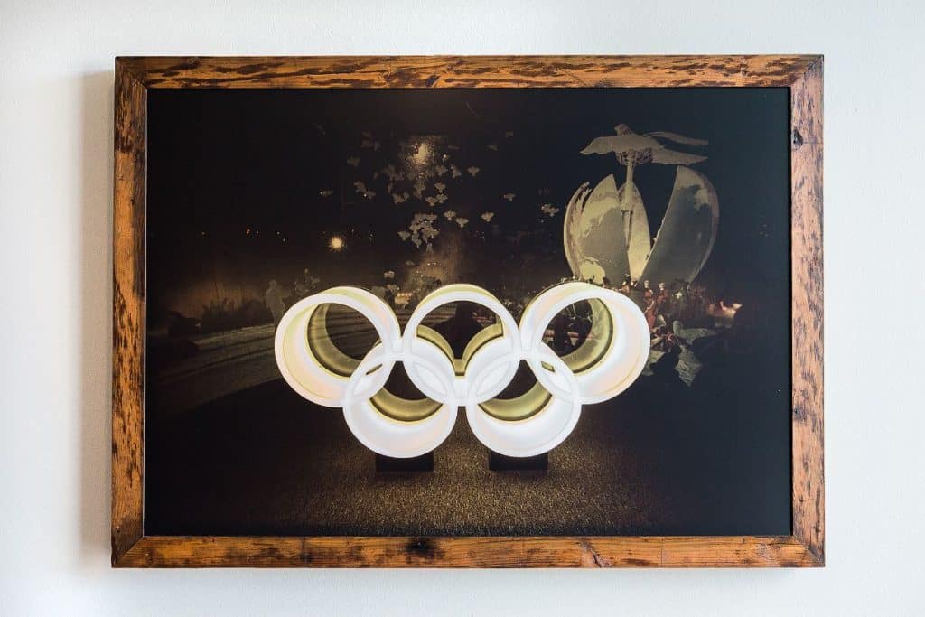 Framed photo of the Olympic rings with a nighttime backdrop, featuring a dove and flame in the background.