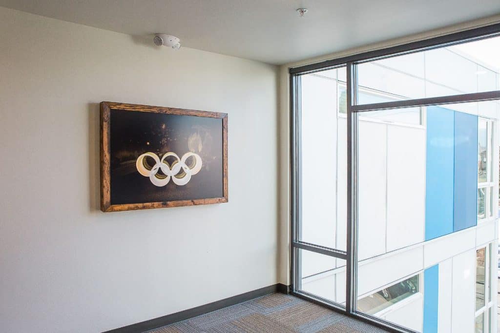 Framed Olympic rings artwork on a light-colored wall near a large window in a modern interior space.