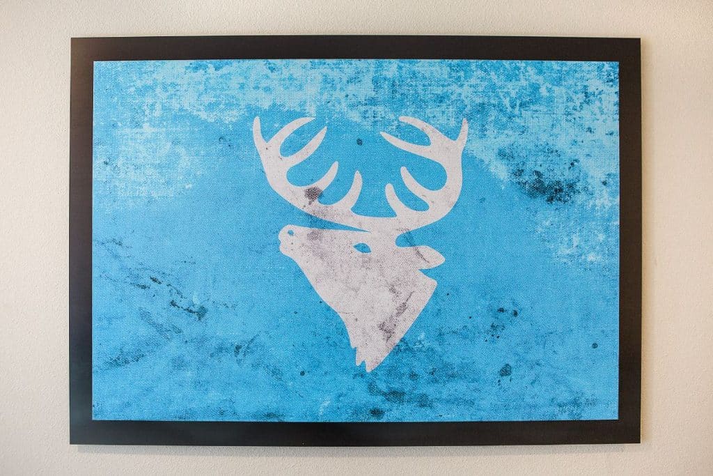 Artwork of a white deer head with antlers on a textured blue background in a black frame.