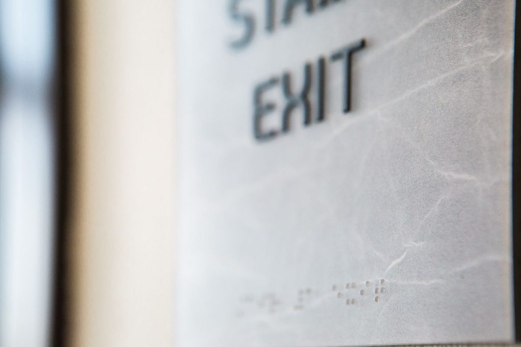 Close-up of a sign with raised Braille text and the partially blurred words "STAIRS EXIT.