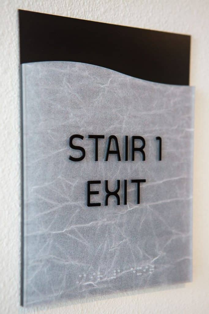 Sign on a wall that reads "Stair 1 Exit" with Braille text beneath it.