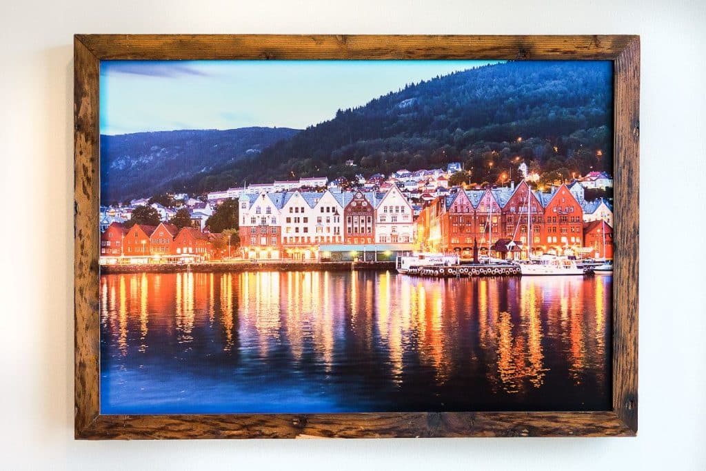 Framed photo of colorful buildings reflecting on water at dusk, set against a hillside under a twilight sky.