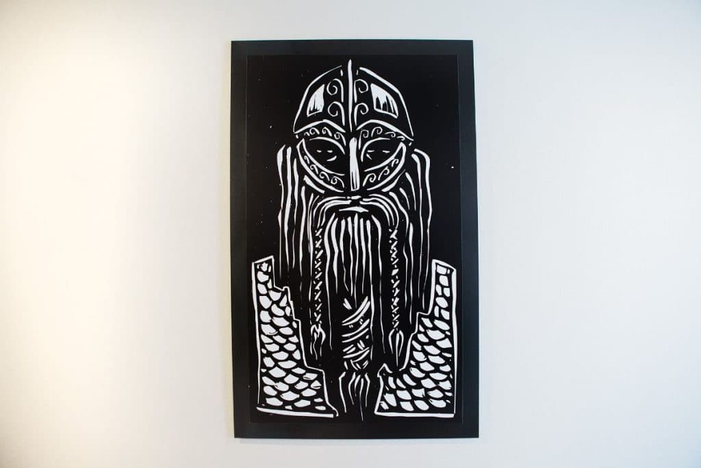 Black and white artwork depicting a stylized, bearded Viking warrior with a helmet, mounted on a wall.