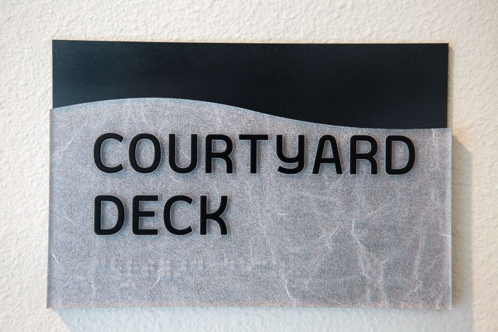 Sign reading "Courtyard Deck" mounted on a textured wall.