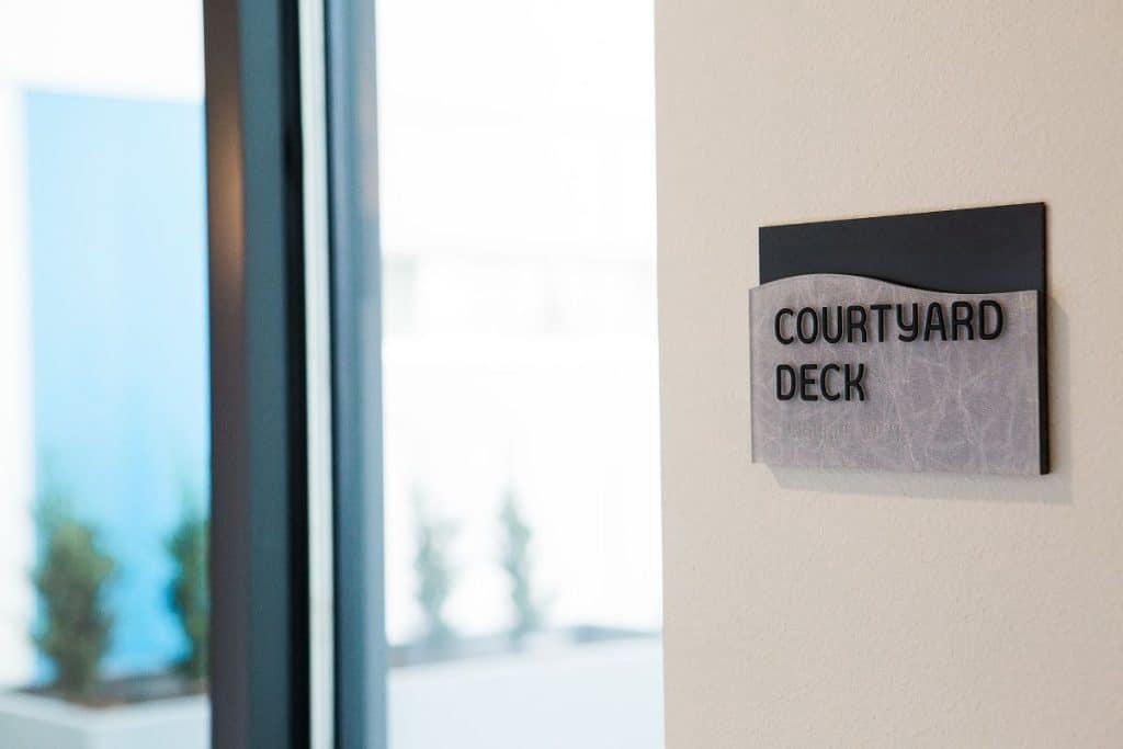 Sign on a wall reads "Courtyard Deck" near a large window with blurred outdoor scenery.