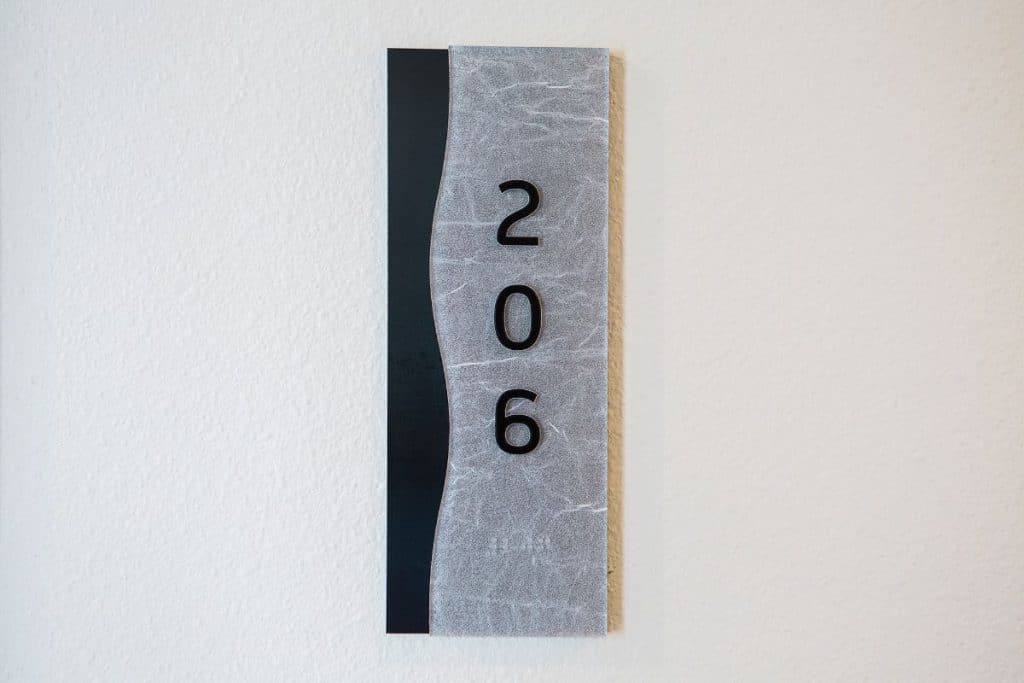 A sign with the number 206 on a textured gray and black background mounted on a white wall.