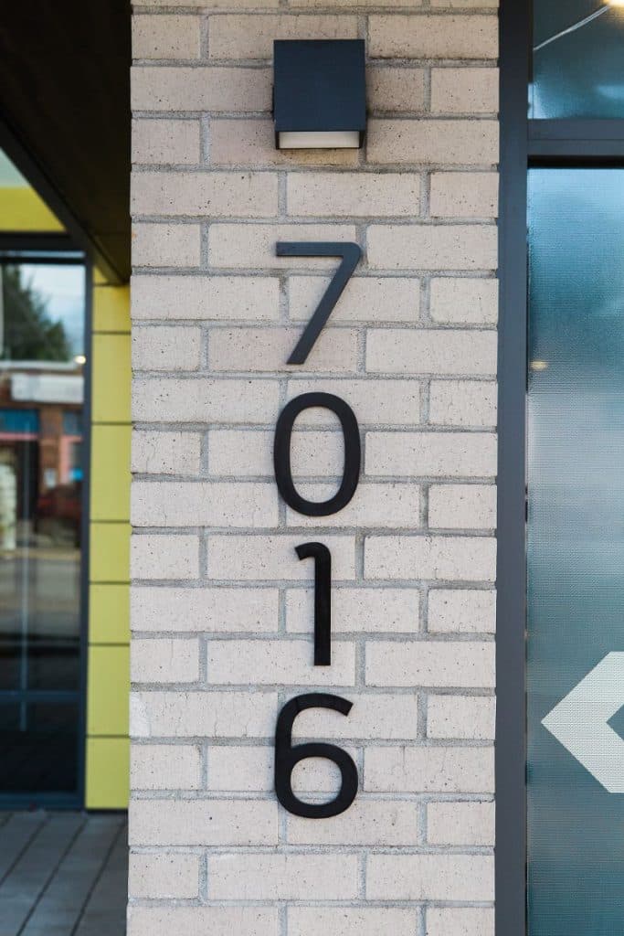 A vertical address number "7016" mounted on a light-colored brick wall.