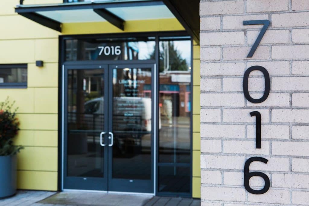 Entrance of a building with glass doors and the number 7016 displayed on a brick wall.