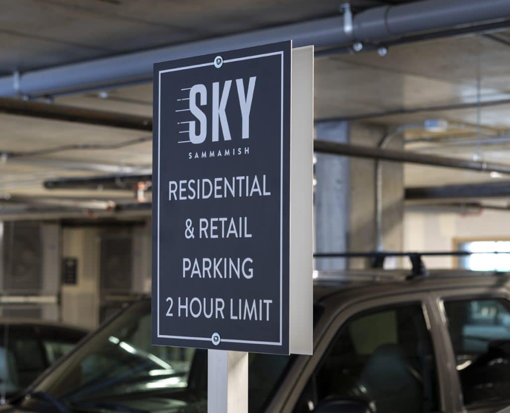 Sign in a parking garage reads: "SKY SAMMAMISH RESIDENTIAL & RETAIL PARKING 2 HOUR LIMIT" with parked cars in the background.