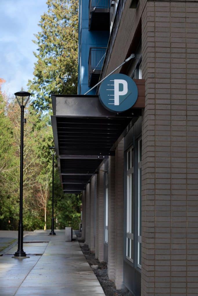 Brick building with a circular "P" parking sign above the sidewalk. Trees and a lamppost are visible in the background.