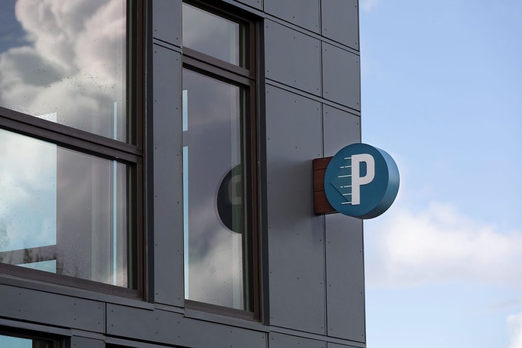 A sign with a "P" symbol, indicating parking, is mounted on the corner of a building with large windows.