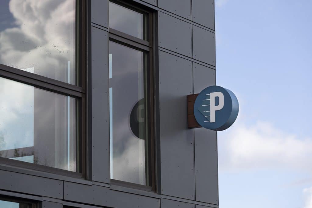 A "P" parking sign is mounted on the corner of a modern building with large windows.