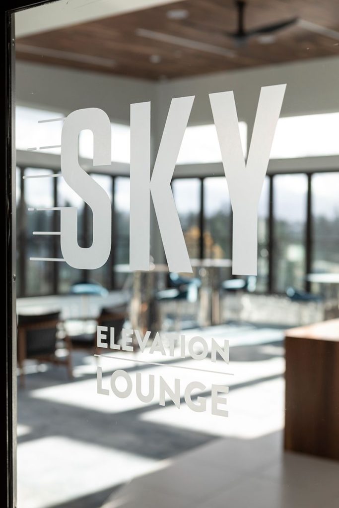 Glass door with "SKY Elevation Lounge" text, revealing a modern interior with large windows and sleek furniture inside.