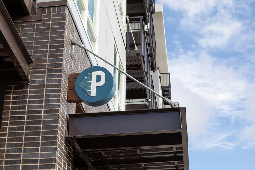 Parking sign mounted on the side of a brick building against a partly cloudy sky.