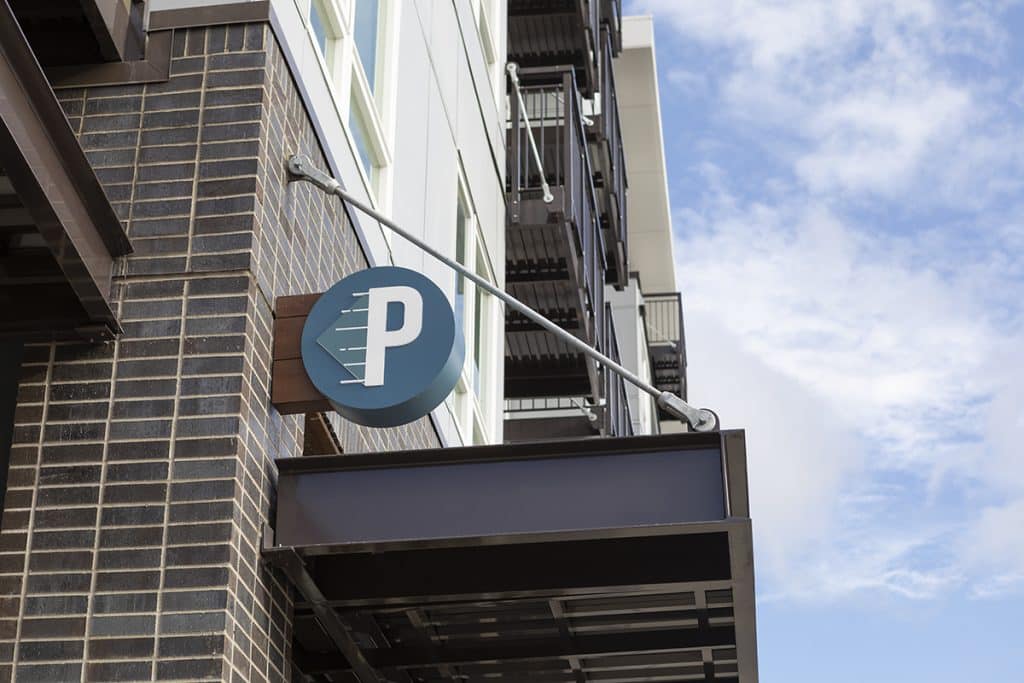 A building exterior with a blue circular sign displaying the letter "P" in white, mounted on a brick wall.