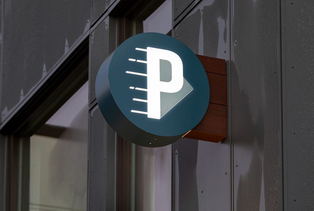 Illuminated parking sign with a letter "P" and an arrow, mounted on a building exterior.