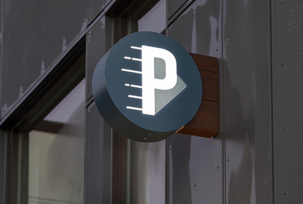 Illuminated parking sign with a large letter "P" on a circular background attached to a building facade.