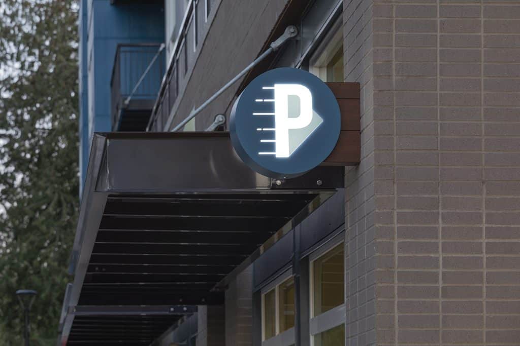 Illuminated parking sign with a letter "P" and measurement lines on the side of a building, under a black awning.