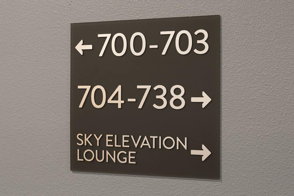 Directional sign on a wall for rooms 700-703 to the left, rooms 704-738 to the right, and Sky Elevation Lounge to the right.