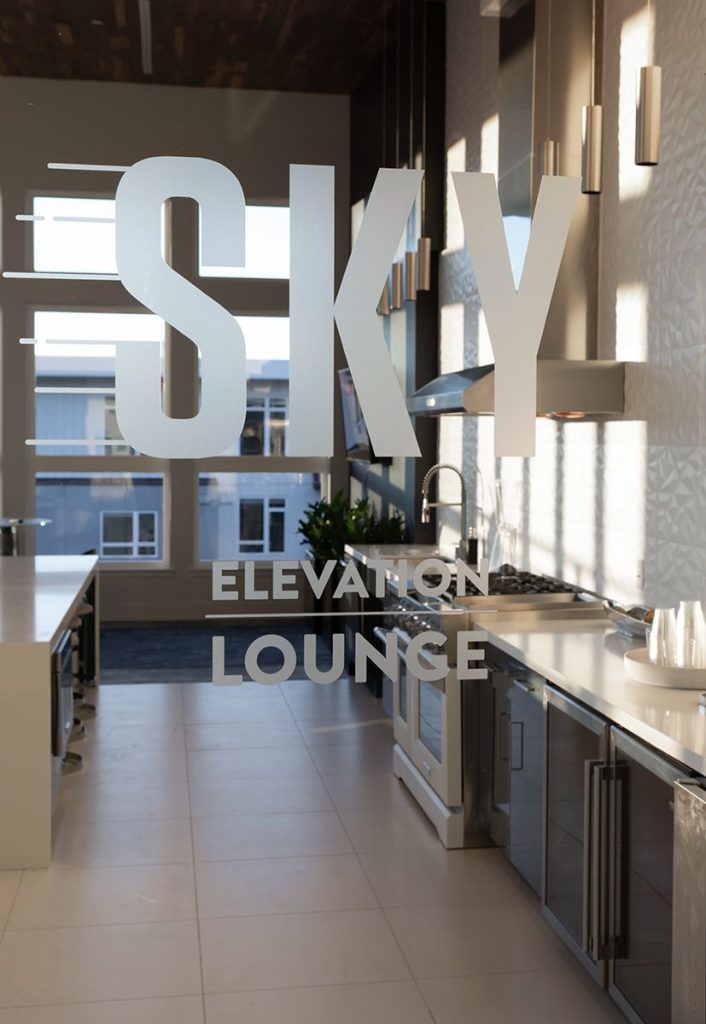 Modern kitchen area with large windows and a "Sky Elevation Lounge" sign on the glass partition.