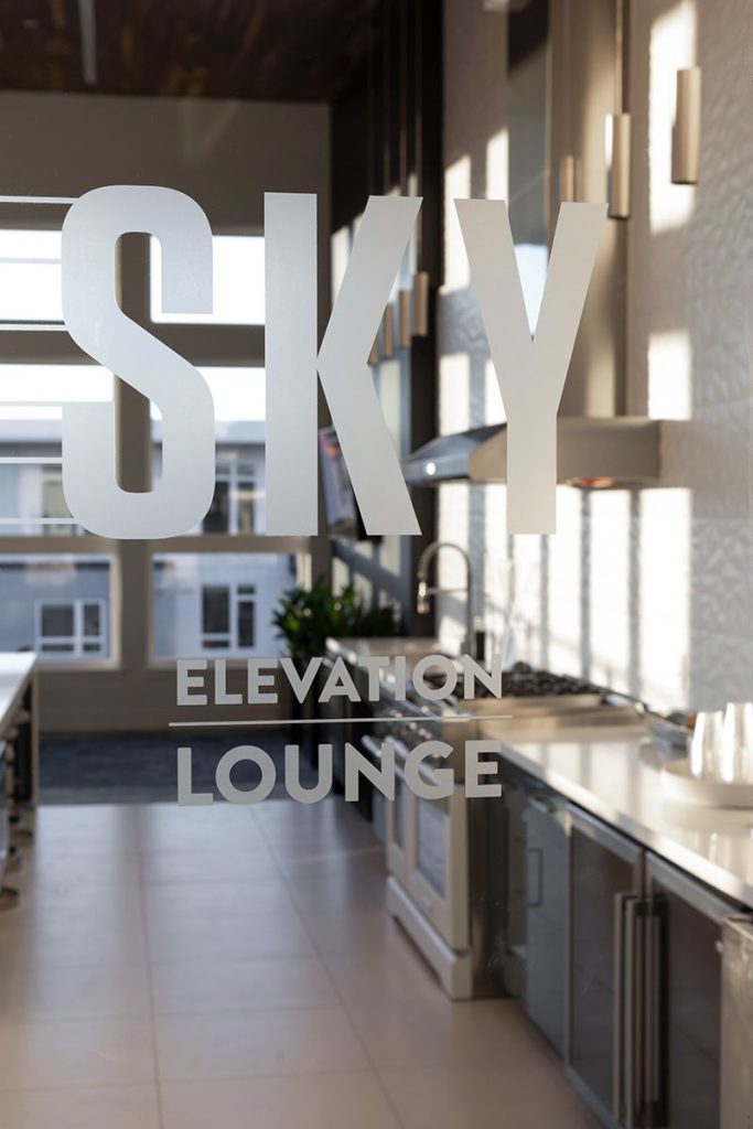 Frosted glass door with "Sky Elevation Lounge" text; modern kitchen interior visible through the glass.