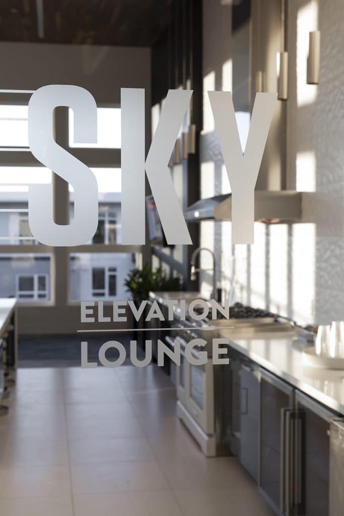 SKY Elevation Lounge" text on a glass door with a view of a modern kitchen interior.