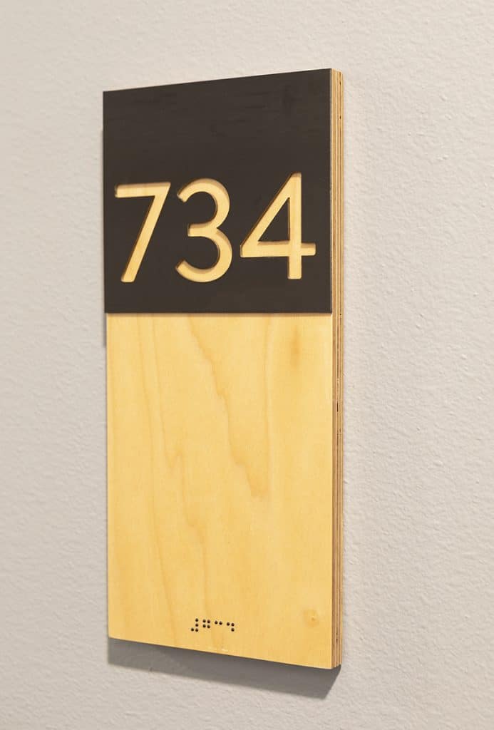 Room number sign displaying "734" in large numbers with Braille underneath on a wood and black background.