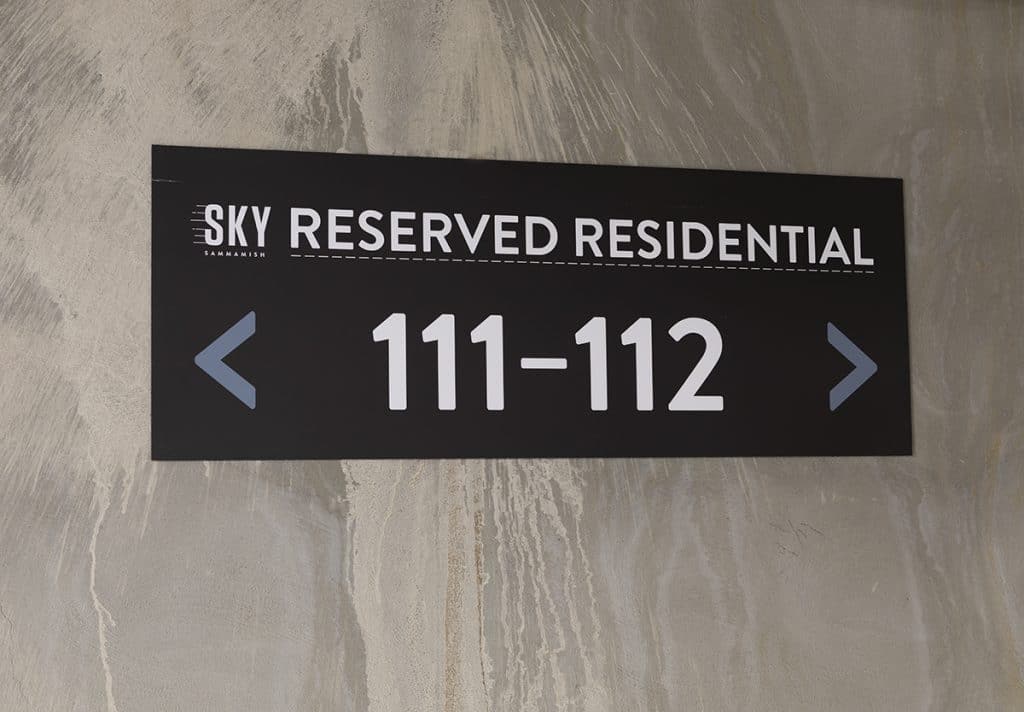 Black sign reading "SKY RESERVED RESIDENTIAL 111-112" with arrows pointing left and right, mounted on a concrete wall.