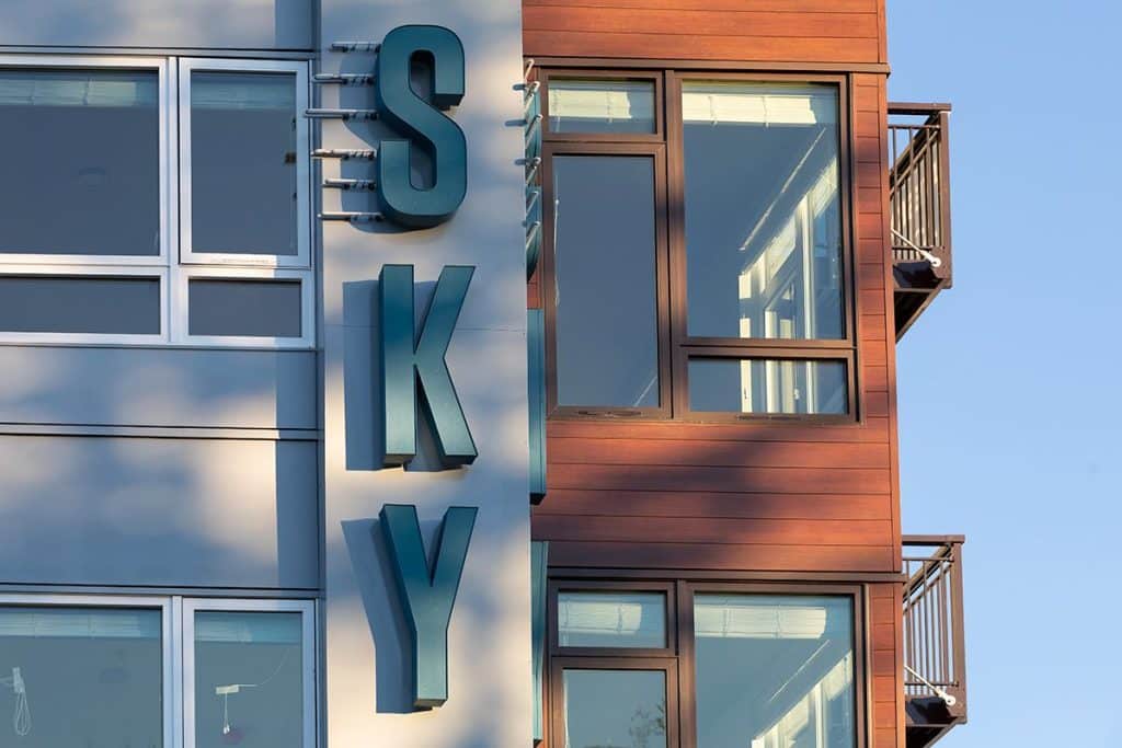 Modern building exterior with large vertical "SKY" sign and large windows under a clear blue sky.