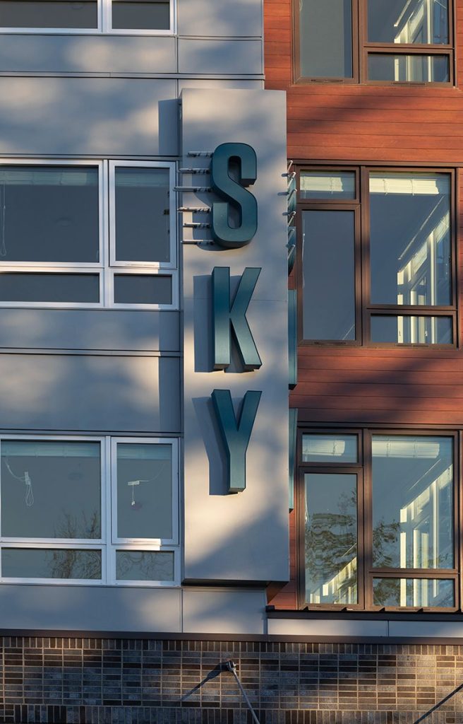 Close-up of a building facade with large letters spelling "SKY" vertically on a sign, next to glass windows and wood paneling.