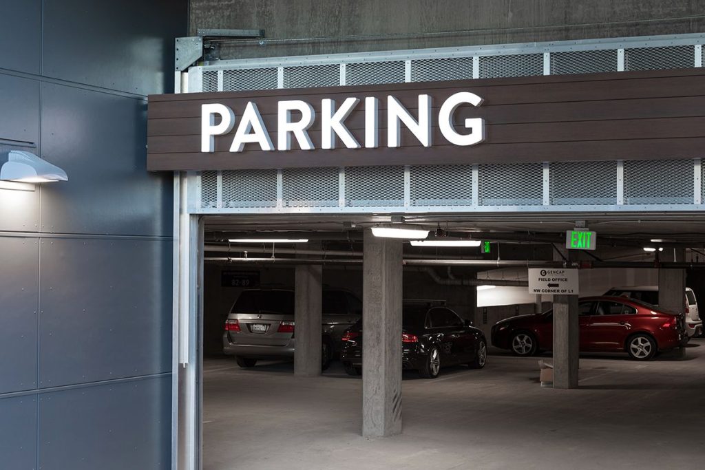 Entrance to an underground parking garage with cars parked inside and a large "PARKING" sign above.