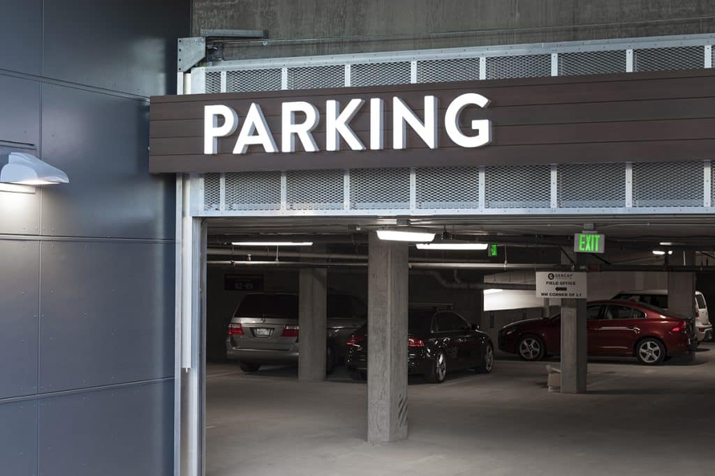 Entrance to a parking garage with illuminated "PARKING" sign and several cars parked inside.