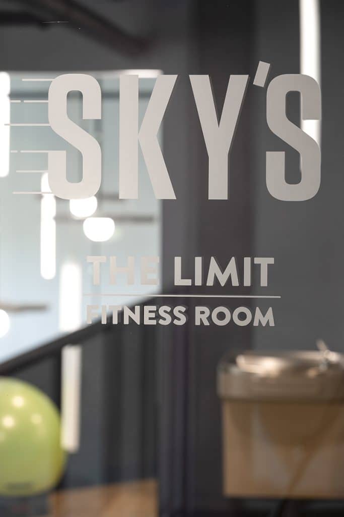 Glass door with the text "Sky's The Limit Fitness Room" visible. A yellow exercise ball and gym equipment are seen in the background.